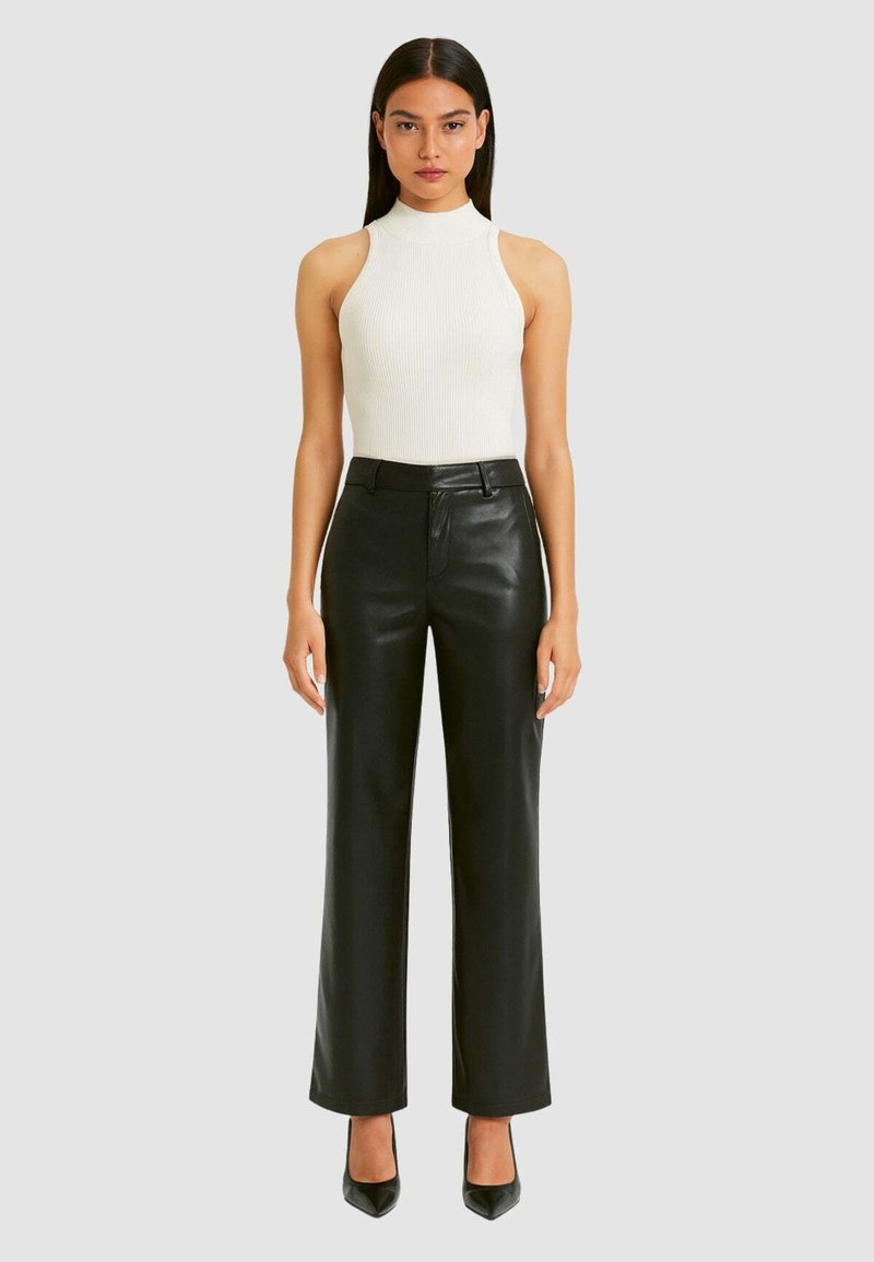Pantaloni larghi in pelle nera con vita alta, abbinati a un top attillato bianco a coste senza maniche. Il modello indossa tacchi neri a punta.