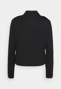 Musta fitted-takki, rakenteellinen muotoilu kauluksella, olkaimilla ja napitusyksityiskohdilla hihoissa. Sileä, tekstuuri kangas.