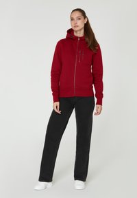Sudadera roja con cremallera hecha de material de sudadera, con capucha, combinada con jeans rectos negros y zapatillas blancas. Diseño simple, logotipos mínimos.