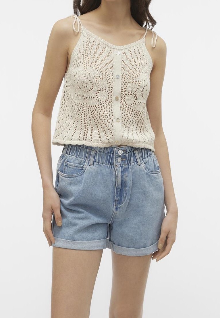 Neulejacket vaaleasta kerma-väristä nappikiinnityksellä ja monimutkaisella pitsikuvioinnilla, yhdistettynä vaaleansinisiin farkkushortseihin, joissa on käännetyt lahkeet ja elastinen vyötärö.