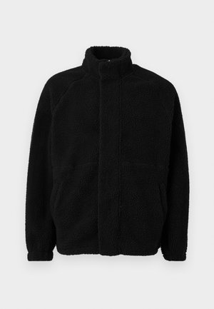 Veste en polaire noire avec col haut, fermeture éclair à l'avant, deux poches latérales, matériau texturé et manches raglan. Design simple et épuré.