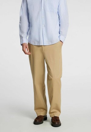 Light blue striped button-up shirt with long sleeves and a chest pocket, paired with beige trousers and brown shoes.