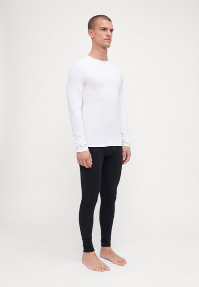 Weißes Langarm-Basisschicht-Oberteil, kombiniert mit schwarzen eng anliegenden Leggings. Die Materialien wirken glatt mit einer engen Passform. Keine sichtbaren Muster oder Logos.