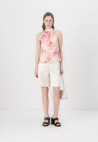 Blomstrete halterneck-top i pastellfarger, kombinert med hvite strukturerte shorts. Har et glatt stoff og svarte hælede sandaler med spenner.