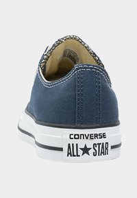Námořnické modré plátěné nízké tenisky s bílou gumovou podrážkou. Na patě je logo "Converse All Star" a kontrastní stehy.