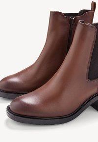 Bottes chelsea en cuir marron avec une finition lisse, des panneaux latéraux élastiques, un petit talon et un design de bout rond. Semelle en caoutchouc noir.