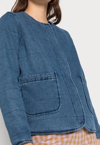 Jeansjacka med kviltad textur, rund halsringning och två framfickor. Färgen är medelblå med något blekta inslag.