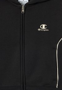 Felpa nera con zip realizzata in tessuto morbido, con un logo crema sul lato sinistro del petto e piping bianco lungo le tasche frontali.