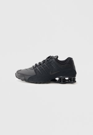 Schwarze Sportschuhe aus strukturiertem Synthetikmaterial, mit einem eleganten Design, sichtbaren Schnürsenkeln und einer markanten segmentierten Sohle mit schwarzen Akzenten.
