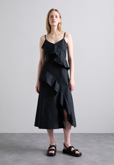 Rochie neagră fără mâneci, cu detalii de volan asimetric și fanta pe lateral. Fabricată dintr-un material neted, are bretele subțiri și un corset adecuat.