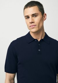 Mörkblå kortärmad polo shirt i mjukt tyg, med krage som stängs med knappar och en strukturerad stickad design.