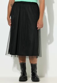 Sort tylskørt med elastik i taljen, knælangt, lagdelt design, båret over sorte kampstøvler med sølvnitter.