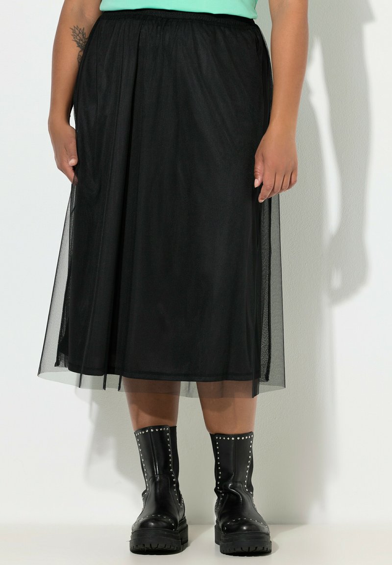 Sort tylskørt med elastik i taljen, knælangt, lagdelt design, båret over sorte kampstøvler med sølvnitter.