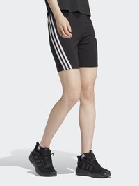 Șorturi atletice negre cu un design cu trei dungi albe pe părțile laterale, asociate cu pantofi sport negri cu partea superioară din plasă și talpă texturată.