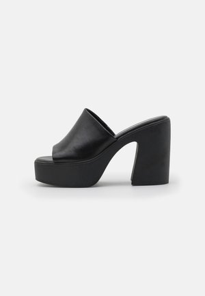 Mule nere con tacco alto, con una parte superiore in pelle liscia e una suola a piattaforma spessa, con punta aperta e design del tacco a blocco inclinato.