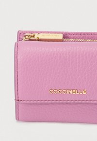 Nærbilde av en teksturert rosa lærvelger med gullglidelås og COCCINELLE-logo i gullbokstaver på fronten.