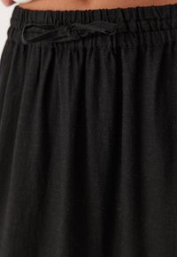 Zwarte rok van lichtgewicht stof. Voorzien van een geplooide tailleband met een trekkoord. Soepele textuur met zachte draping en geen patronen.