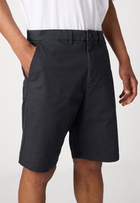 Black cotton shorts with a button closure, side pockets, and a straight leg design. The fabric has a smooth texture and minimal detailing.