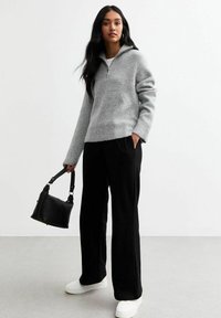 Grijs geribbeld sweater met een halve rits kraag, gecombineerd met zwarte wijde broek en witte sneakers. Houdt een zwarte handtas vast.