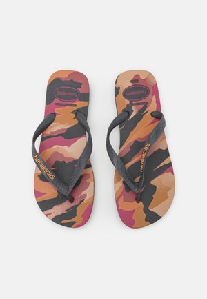 Paire de tongs avec des brides noires et des semelles au motif camouflage orange, rose et noir, avec le logo Havaianas sur les brides.