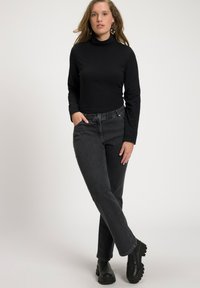 Jersey negro de manga larga con cuello de tortuga combinado con jeans oscuros de cintura alta. El modelo lleva botas negras hasta el tobillo; accesorios mínimos. Fondo simple.