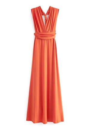 Femme portant une robe maxi orange sans manches avec un détail croisé, tenant une pochette beige, debout contre un mur blanc à panneaux.