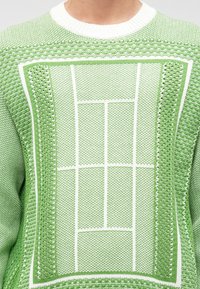 Pull en tricot vert avec un design texturé et des motifs géométriques blancs. Col ribbed blanc et détails de couture élaborés.