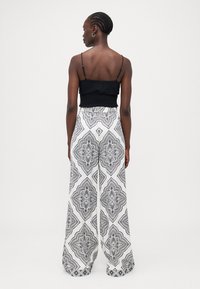 Top corto negro fruncido con tirantes finos, combinado con pantalones de pierna ancha blancos que tienen intrincados patrones geométricos negros.