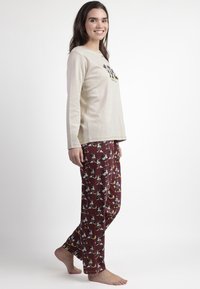 Camisa de pijama de manga larga beige con detalle de botones, combinada con pantalones color marrón con un patrón de dibujos animados de personajes y acentos brillantes.