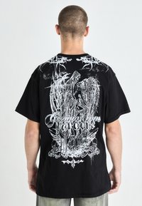 Black cotton t-shirt with a large white graphic on the back featuring the text "Greetings from Paradise" and intricate designs.