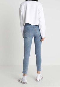 Person wearing light blue skinny jeans, white cropped sweatshirt, and white high-top sneakers, standing against a plain light background.