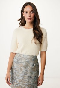 Pull créme, léger et moelleux à manches courtes associé à une jupe bleu clair présentant un motif abstrait texturé dans des tons dorés et bleus.