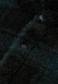 Tissu en polaire texturé noir et sarcelle avec une surface douce et moelleuse. Présente un motif à carreaux audacieux et des détails de boutonnières visibles.