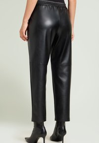 Zwarte faux leren broek met een ontspannen pasvorm, voorzien van een hoge elastische tailleband en naaddetails, gecombineerd met strakke zwarte enkellaarsjes.