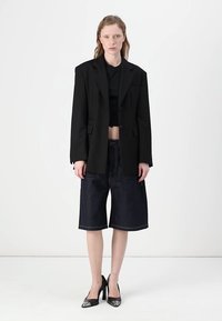 Črn oversized blazer, skrajšan črn top, temno denim kratke hlače širokega kroja in črne koničaste pete. Preprost dizajn z nasprotujočimi si teksturami.