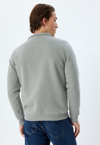 Felpa grigia con un design semplice, colletto e polsini a coste, e una forma aderente, abbinata a jeans in denim blu. Texture semplice.