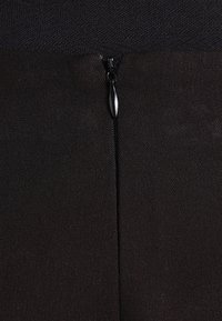 Prenda de tela negra con cierre central de cremallera, de textura suave y diseño minimalista. El tirador de la cremallera es redondeado y metálico.