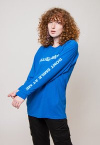 Bright blue long-sleeve t-shirt made of soft fabric, featuring white text on sleeves. Relaxed fit with a crew neckline and straight hem.