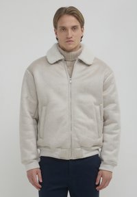 Giacca bomber beige con zip, colletto peloso bianco, polsini elasticizzati e tasche laterali. Tessuto morbido e vestibilità rilassata con finitura liscia.