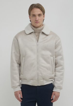 Giacca bomber beige con zip, colletto peloso bianco, polsini elasticizzati e tasche laterali. Tessuto morbido e vestibilità rilassata con finitura liscia.