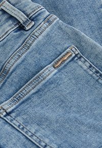 Heled sinine denimpind, millel on nähtavad õmblused; sisaldab taskut metallaktsendiga. Materjalil on veidi kulunud tekstuur.