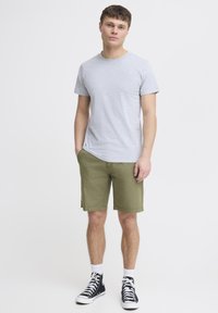 Graues Baumwoll-T-Shirt kombiniert mit olivgrünen Shorts, die einen klassischen Schnitt und Seitentaschen haben, ergänzt durch schwarze High-Top-Sneaker.