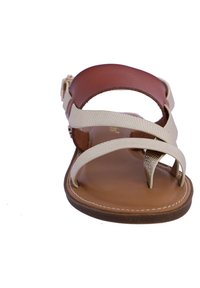 Sandalía en tonos marrón claro y beige con una tira de cuero suave, bandas elásticas texturizadas y un diseño de puntera dividida con una suela plana.