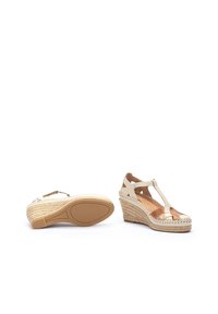 Sandales compensées beiges avec un design à lanière en T et des découpes, semelle intermédiaire en jute tressé et accents marron texturés. Dessus en cuir lisse avec couture.
