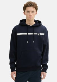 Sudadera azul marino hecha de un tejido suave, con dos franjas horizontales blancas, un bolsillo tipo canguro y capucha con cordón.
