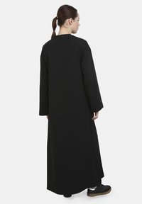 Svart långärmad klänning med rak skärning, minimalistisk design och slät textur, matchad med svarta sneakers och en neutral bakgrund.