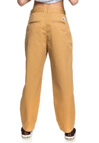 Béžové kalhoty s širokým střihem a hladkou texturou, se zadními kapsami a štítkem, navržené pro uvolněný fit.