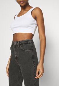 Vit ribbad crop top med vida axelremmar, matchad med högmidjade mörkgrå jeans med slitdetalj fram.
