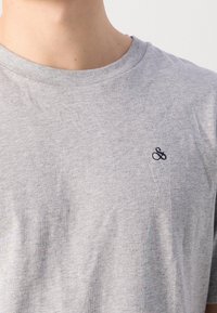 Grijze katoenen t-shirt met een ronde halslijn en korte mouwen, voorzien van een klein marineblauw "&" logo op de linkerkant van de borst.