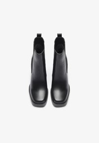 Bottines en cuir noir avec une finition lisse, bout carré, panneaux élastiques sur les côtés et languettes pour un enfilage facile.
